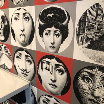 Hawt Pizza Co. - The image shows a wall decorated with a grid of circular black-and-white images. These images include various faces with different expressions, a skull, a snake, a city street scene, and a woman with a map overlay. The background colors alternate between red, gray, and white, creating a patterned display. The wall appears to be part of an interior space, possibly an art installation or decorative feature. - Pizza Near Me - Albuquerque, New Mexico