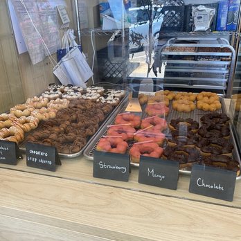 T% Coffee + Tea - Davis  - A glass display case contains various donuts labeled with flavors like strawberry, mango, and chocolate, along with cookies and churros. - Bubble Tea Near Me - Davis, California