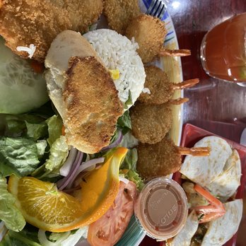 Las Islitas Stone Park - Breaded shrimp - A plate contains breaded shrimp arranged around a serving of white rice topped with a small yellow garnish. The dish is accompanied by a side salad with lettuce, tomato, onion, and orange slices. A small container of dipping sauce is also on the plate. The meal is served on a colorful, patterned plate, with a fork and a glass of iced tea nearby. - Mexican Near Me - Stone Park, Illinois