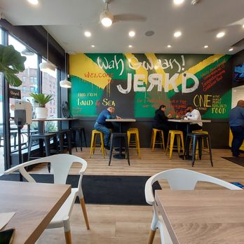 Jerk'D - Inside - Inside Jerk'D, a Caribbean restaurant, with customers sitting at tables near a vibrant mural and large windows. - Caribbean Near Me - Hackensack, New Jersey
