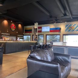 The bar - Casper Brewing Company interior featuring a bar with stools, leather seating, and flags on the wall, including the Colombian and Bavarian flags.