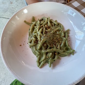 Pastamarket - Pistachio - Strozzapreti Mascar - A white bowl contains green pasta, garnished with crushed nuts and seasoning, on a table at an Italian restaurant. - Italian Near Me - Miami, Florida