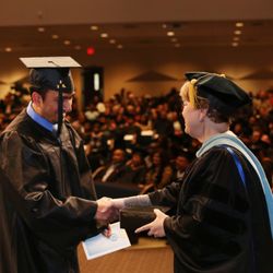 Amberton University - A faculty member congratulates a graduate on stage during Amberton University's commencement ceremony as a packed auditorium looks on.