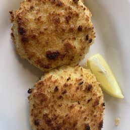 Crab Cakes - Two golden-brown crab cakes are served on a white plate with a lemon wedge for garnish.