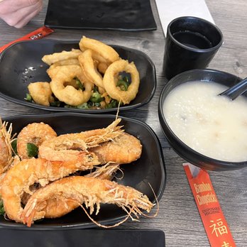 IT DIMSUM - Squid with Salt and Pepper, Salt and Pepper Shrimp and Pork Porridge - The image shows a meal with fried shrimp, onion rings, congee, and a dark beverage on a wooden table, with chopsticks and a business card nearby. - Dim Sum Near Me - Albuquerque, New Mexico