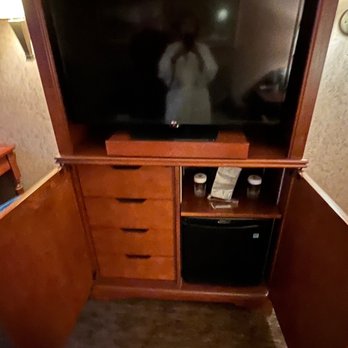 Hotel Captain Cook - Small fridge and drawers with ice bucket beneath 1 of 2 televisions - Hotels Near Me - Anchorage, Alaska