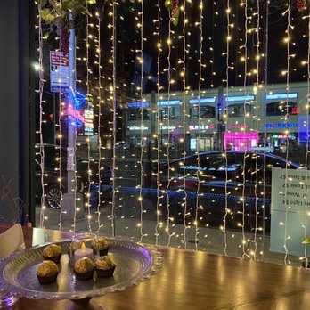 Firefly - Nighttime scene inside a restaurant with a window decorated with string lights and grapevine garland, overlooking a busy street with neon signs. - Cocktail Bars Near Me - Flushing, New York