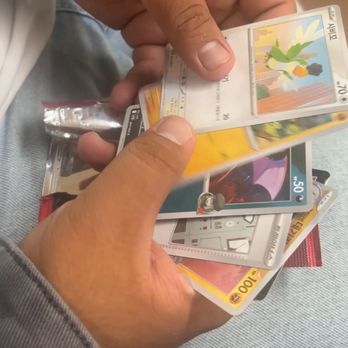 Oppa's - A person is holding several Pokémon trading cards, with some cards visible showing characters and artwork. - Toy Stores Near Me - Westminster, California