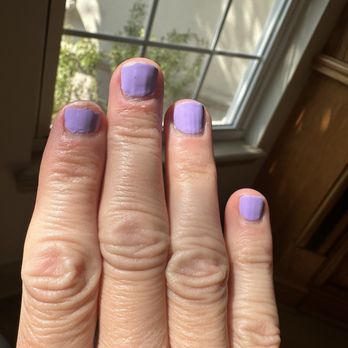 Queen Nails - So many chips in so little time - The image shows a hand with four fingers visible, each with purple nail polish that appears slightly chipped. The hand is held up close to a window with grid panes, allowing natural light to illuminate the scene. The background includes part of a wooden cabinet and a wall outside the window, with some greenery visible through the glass. - Nail Salons Near Me - St. Augustine, Florida