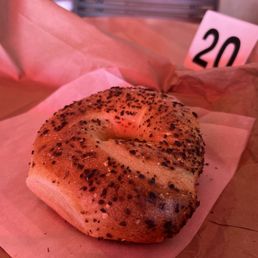 Onion Bagel - A bagel topped with sesame seeds and black seasoning, resting on parchment paper on a wooden surface.