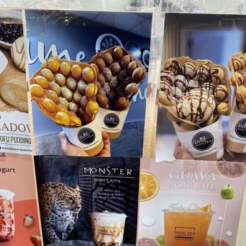 Ding Tea Rolling Meadows - Collection of promotional posters at Ding Tea Rolling Meadows showcasing various bubble tea drinks, bubble waffles, and desserts. The posters feature images of bubble waffles topped with toppings like caramel balls and chocolate drizzle, along with flavored teas such as guava and monster bo bo latte. The posters are arranged on a display board, highlighting menu items and visual appeal of the desserts and beverages. - Bubble Tea Near Me - Rolling Meadows, Illinois