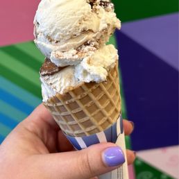 Chocolate Taco Icecream Cone - A person holds a waffle cone with two scoops of vanilla ice cream containing chocolate chips, with a colorful, patterned background.