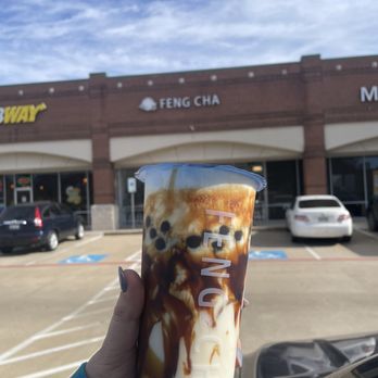 Feng Cha Coppell - Dirty boba! - A person holds a milk tea with caramel syrup and tapioca pearls outside Feng Cha Coppell, with the storefront visible in the background. - Bubble Tea Near Me - Coppell, Texas