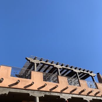 SkyFire - Then restaurant is up the path to the top floor of this building. - A two-story building with a terracotta-colored exterior, featuring a wooden pergola on the upper balcony and decorative metal railings. - American Near Me - Santa Fe, New Mexico