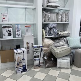 Shambles - Home decor and bedding items such as pillows and comforters are arranged on shelves, with Shark vacuum cleaners in boxes on the floor.
