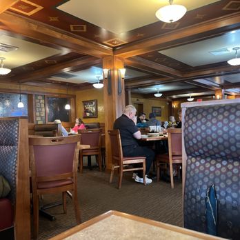 Superior Restaurant - The image shows the interior of a restaurant with wooden ceiling beams and decorative ceiling panels. Several ceiling lights illuminate the space, and patrons are seated at tables, some engaged in conversation or dining. The walls are painted yellow and decorated with framed artwork. The furniture includes wooden chairs and booths with patterned upholstery. The overall atmosphere appears cozy and inviting. - Diners Near Me - Emmaus, Pennsylvania