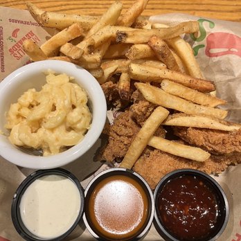 Chili's - Great Chicken Strips and Fries with sub-par mac&cheese - The image shows a tray with French fries, fried chicken tenders, and a small bowl of macaroni and cheese. Three small cups contain different dipping sauces: one appears to be ranch, another possibly honey mustard, and the third a barbecue or similar sauce. The food is served on restaurant paper with a wooden table background. The presentation suggests casual dining, with a focus on fried comfort foods. - American Near Me - Mesa, Arizona