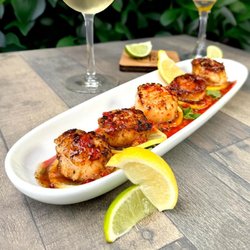 Pan seared scallops on arugula with lemon and Thai chili sriracha drizzle. Elegant seafood in Modesto.