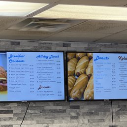Menu - Digital menu screens show breakfast croissants, all-day lunch sandwiches, and various donuts and kolaches at a bakery or cafe.