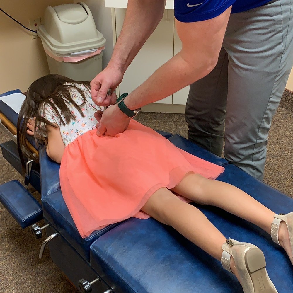 Schilsky Chiropractic - Pretending to pop her back by clicking something along her back. - Chiropractors Near Me - Jacksonville, North Carolina