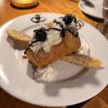 Nova Pizzabar - A fried pastry dessert topped with whipped cream, blackberries, and chocolate syrup, served on a white plate with biscotti and powdered sugar. - Pizza Near Me - Larchmont, New York