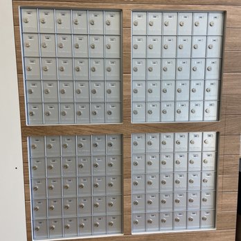 The UPS Store - A wall-mounted mailbox system features four sections of gray metal mailboxes, each with individual compartments secured by locks. The top left section has 40 mailboxes, the top right has 36, the bottom left has 40, and the bottom right has 36, totaling 152 compartments. The mailboxes are labeled with numbers, and a sign reading '24 Hour Mailboxes' is positioned above the system. The background consists of horizontal wood paneling, providing a clean and organized appearance. - Shipping Centers Near Me - Antelope, California