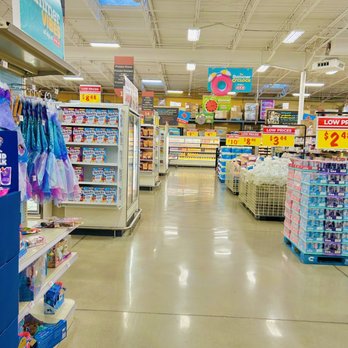 H-E-B - Inside - Inside a grocery store, shelves are stocked with various products, including frozen foods and snacks, with price signs visible. A shopping cart with items is in the foreground. - Grocery Near Me - Killeen, Texas