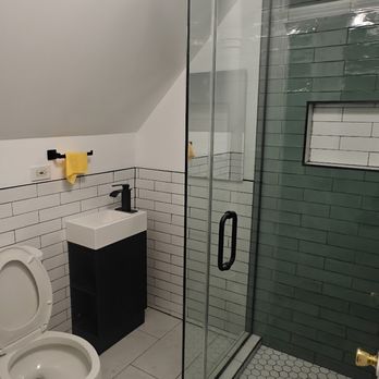 Premier Remodeling Services - A bathroom featuring a toilet, a small black and white sink, and a glass shower with green tiles and hexagonal floor tiles. - Flooring Near Me - Morton Grove, Illinois