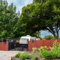 Skyline RV Park - RV living beneath a canopy of trees, with an individual gate, wooden fencing, and flowering plants beside the site.