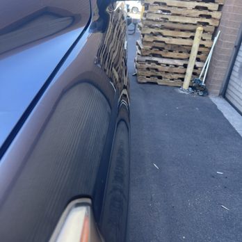 Finesse Pros - Front fender after. Dent is bye bye. - The image shows the side of a dark-colored vehicle with a highly reflective surface, capturing reflections of nearby structures and objects. - Mobile Dent Repair Near Me