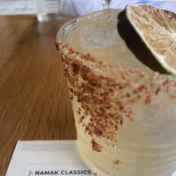 Namak - A close-up of a cocktail with a lime wedge garnish and chili powder rim, placed on a wooden table at a restaurant. - Mediterranean Near Me - Washington, DC, District of Columbia