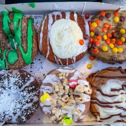 1/2 dozen donuts - A box contains six donuts with different toppings, including colorful candies, icing, and drizzles, from a donut shop.