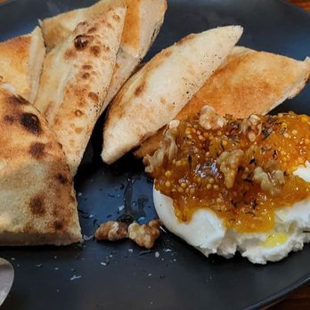 Sofia - A black plate holds naan bread, mashed potatoes topped with gravy and nuts, with a glass of water nearby on a wooden table. - Italian Near Me - New Orleans, Louisiana