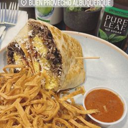 Breakfast Burrito with bacon - A breakfast burrito filled with shredded beef, cheese, and eggs, accompanied by fried onion strings and a side of salsa, at Buen Provecho Albuquerque.