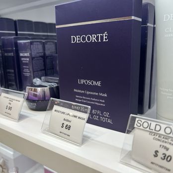 Maison Kose - The image shows a retail display of Decorté Liposome Moisture Liposome Mask boxes on a store shelf. The boxes are dark purple with white text, and there are price tags in front indicating the cost for six masks and individual units. The shelf also contains other skincare products, with a clean, organized presentation typical of a beauty or skincare store. - Cosmetics & Beauty Supply Near Me - Arcadia, California