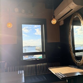 Diego's - A restaurant interior features a window with a view of a waterfront, with outdoor seating visible outside. The room has hanging light bulbs, a large ornate mirror, and an air conditioning unit. - Mexican Near Me - Newport, Rhode Island