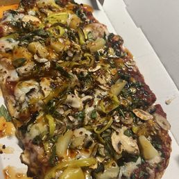Custom Vegan Pizza w honey sriracha drizzle - A rectangular vegan pizza with a variety of toppings including mushrooms, green peppers, herbs, and a honey sriracha drizzle, served in a white pizza box.