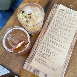 Red Flannel and Mullhouse - Two drinks with ice and garnishes sit on a wooden table next to a menu from Wildly Crafted.
