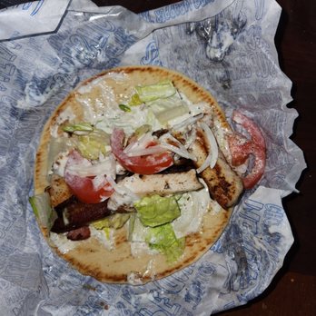 Gyro Shack - Chicken bacon ranch gyro. Awesome - A partially eaten gyro featuring lettuce, tomato slices, onion, and grilled meat on a flatbread. The gyro is placed on branded paper, with a fork visible at the edge of the image. The background includes a dark wooden surface and a plastic container. The image captures the food in a casual dining setting. - Greek Near Me - Albuquerque, New Mexico