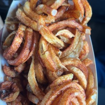 Big Ass Burgers - Curly fries - A close-up of fried curly fries served in a paper container, likely from a takeout spot, with a background of a vehicle interior. - Fast Food Near Me - Thoreau, New Mexico