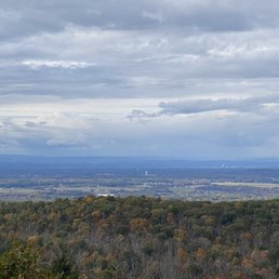 A scenic landscape showing a forest with trees in fall colors, distant mountains, and a cloudy sky overhead.