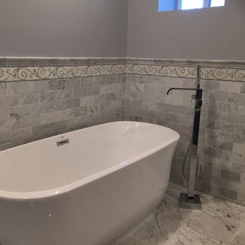 Loti Contracting - After picture - newly installed tub and faucet - A bathroom features a white freestanding bathtub with a sleek design, tiled walls with decorative border, and a wall-mounted shower fixture. A small window provides natural light. - General Contractors Near Me - Briarcliff Manor, New York