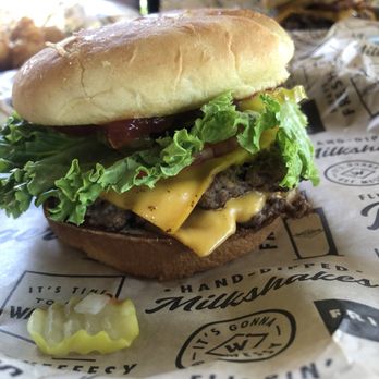 Wayback Burgers - Classic burger. - A cheeseburger features lettuce, tomato, pickles, melted cheese, and a beef patty in a sandwich bun, served on branded paper. - American Near Me - Eugene, Oregon