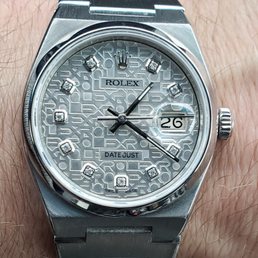 Oysterquartz Restored - A close-up image of a Rolex Datejust wristwatch with a silver dial that has a textured pattern and diamond hour markers. The watch displays the date at 3 o'clock with a magnifying lens and has three hands indicating hours, minutes, and seconds. The watch case and bracelet are made of stainless steel, and the crown is positioned on the right side of the case. The dial includes the Rolex logo and the words 'DATE JUST' and 'SWISS MADE.'