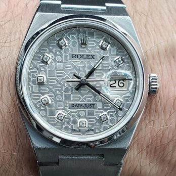 Official Time Watch - Oysterquartz Restored - A close-up image of a Rolex Datejust wristwatch with a silver dial that has a textured pattern and diamond hour markers. The watch displays the date at 3 o'clock with a magnifying lens and has three hands indicating hours, minutes, and seconds. The watch case and bracelet are made of stainless steel, and the crown is positioned on the right side of the case. The dial includes the Rolex logo and the words 'DATE JUST' and 'SWISS MADE.' - Watch Repair Near Me - Sandy, Utah