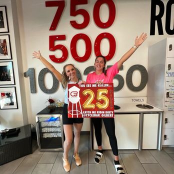 CYCLEBAR - Two women stand inside a fitness or cycling studio, holding a sign that reads '25' and 'Catch me ridin dirty.' They are smiling with arms raised. - Gyms Near Me - Gilbert, Arizona