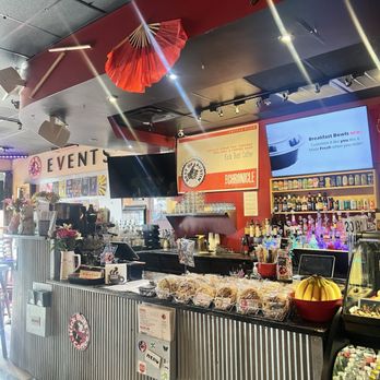 Kick Butt Coffee - Counter - Inside Kick Butt Coffee, a counter displays baked goods, beverages, and decor including umbrellas and flowers, with menu screens overhead. - Coffee & Tea Near Me - Austin, Texas