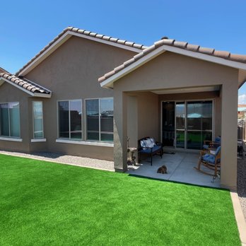 AMG Landscape - Turf and rock fill around the covered patio. - Residential backyard featuring artificial grass, a covered patio with seating, and a small dog on the concrete slab. - Irrigation Near Me