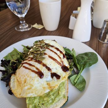 Borealis - Avacado toast - A plate of avocado toast with a fried egg, pumpkin seeds, and balsamic glaze, served with mixed greens at a restaurant table. - Diners Near Me - Aurora, Colorado
