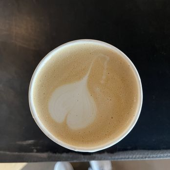 Corvus Coffee Roasters - Vanilla latte - A vanilla latte in a paper cup with latte art on the foam, seen from above on a dark surface. - Coffee & Tea Near Me - Arvada, Colorado